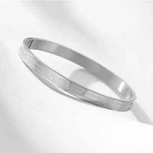 Macro shot of silver stainless steel bangle with Greek key pattern and secure side clasp