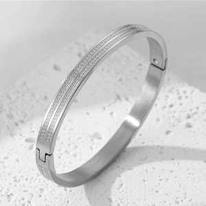 Detailed close-up of silver steel bangle featuring Greek Key engraving and side hinge