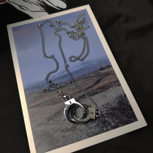 Collier en acier titane argenté avec pendentif menottes poli et gravures thématiques