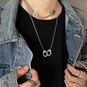 Détail du collier argenté multicouche avec pendentifs menottes et visage triste