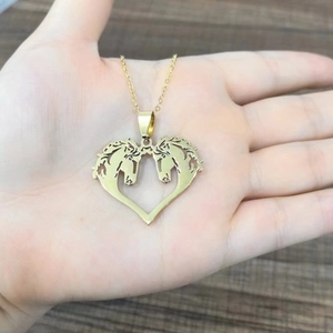 Golden stainless steel heart pendant necklace with double horse heads held in palm