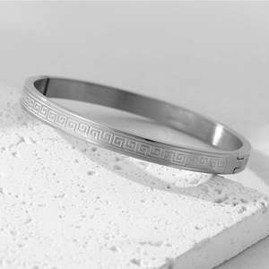 Macro detail of silver stainless steel bangle showing Greek key pattern and hinge closure