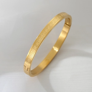 Macro view of gold titanium steel bangle featuring Greek key pattern and side clasp