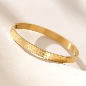 Macro detail of gold stainless steel bangle featuring Greek Key geometric engraving