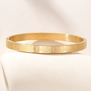 Macro shot of gold stainless steel bangle with geometric fret pattern engraving