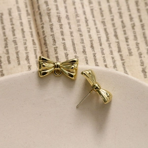 Detailed view of gold ribbon bow earrings and charms on a vintage aesthetic background