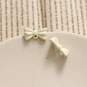 Macro shot of matte cream bow earring studs and jewelry pendant components with metal pins