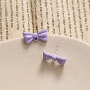Macro detail of purple matte bow earrings with small hanging loop on a vintage fabric