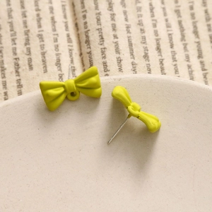 Detailed macro shot of bright yellow matte bow earrings on a vintage textured tray