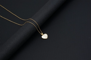 Golden heart necklace with shell inlay and metal letter E on a black background