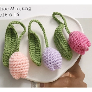 Handmade crochet tulip flower pendants in pink and purple colors on a white ceramic tray