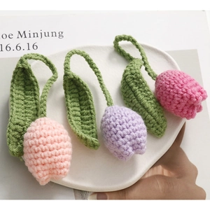 Handmade crochet tulip flower keychain pendants in pink and purple colors on a white tray