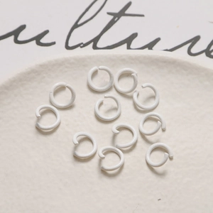 Dettaglio di anellini in metallo bianco macaron per gioielli fai-da-te su vassoio beige