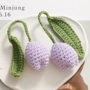 Close-up of hand-knitted lavender tulip pendants with green leaves on a white ceramic plate