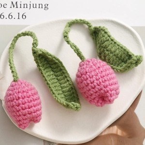 Detail of pink hand-knitted tulip bag charm with green leaf on a white stone tray