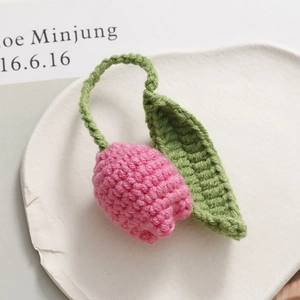 Macro shot of handmade crochet pink tulip with green leaves on a white ceramic plate