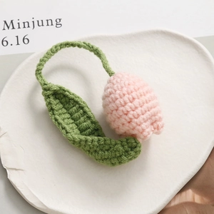 Detailed close-up of handmade pink knitted tulip flower bud with green leaves and stem