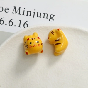 Detail of two yellow ceramic cat charms with hand-painted stripes for DIY jewelry crafts