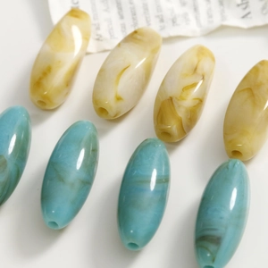 Dettaglio macro di perle ovali marmorizzate in acrilico giallo e turchese per gioielli fai-da-te