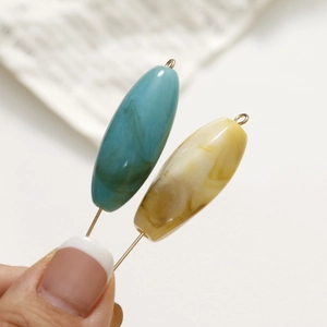 Dettaglio macro di perle in resina effetto marmo ovale con perni dorati per gioielli fai-da-te