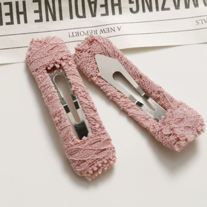 Close-up of pink lace-covered metal snap hair clips showing delicate fabric texture