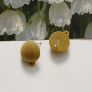 Close-up of mustard yellow flocked round stud earrings with a matte velvet finish