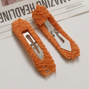 Detailed close-up of orange lace fabric wrapped metal hair clips on newspaper background