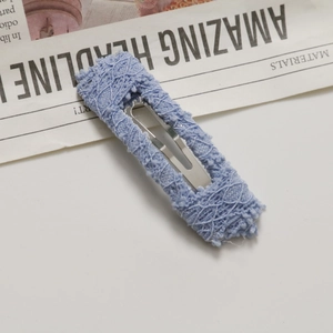 Detail view of a light blue lace-wrapped BB hair clip placed on newspaper