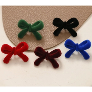 Flocked velvet bow earrings in five colors on a textured leather and cream background