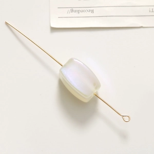 Macro shot of rectangular pearlescent bead with gold metal pin for jewelry making
