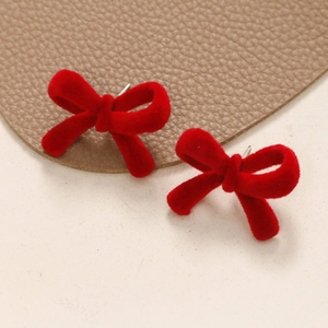 Close-up of red flocked velvet bow stud earring with metallic needle on leather surface