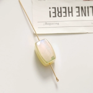 Macro view of a rectangular iridescent bead on a golden metal pin for DIY jewelry making