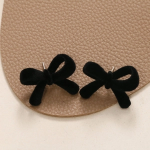 Macro shot of black velvet flocked bow stud earrings on brown leather background
