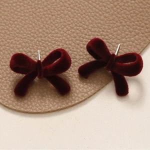 Close-up of velvet bow earrings in burgundy red with detailed flocking texture