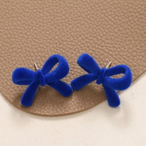 Detail view of Klein blue flocked bow earrings on a textured brown leather background