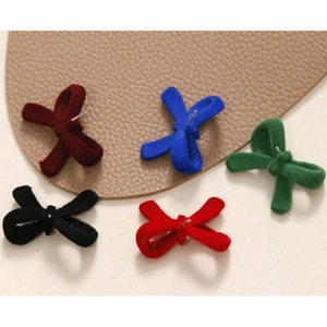 Detailed view of flocked velvet bow earrings in five colors on a leather texture background