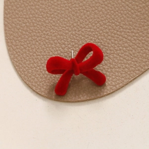 Macro view of a red flocked velvet bow earring stud with metallic pin on leather background