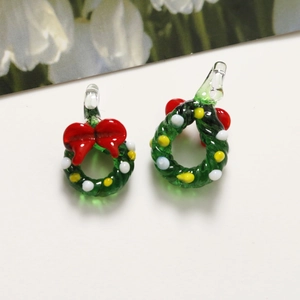Close-up of green glass Christmas wreath charms with red bows and festive details
