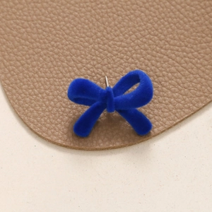 Macro view of dark blue flocked velvet bow earring with silver needle on leather background