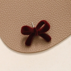 Detailed view of dark red flocked velvet bow earrings on premium leather texture