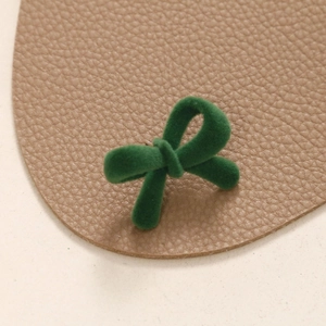 Macro shot of emerald green flocked bow accessory on a textured pebble leather background