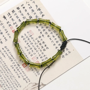 Dettaglio di perline in resina verde a forma di bambù su cordino nero con calligrafia