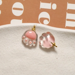 Close-up of pink translucent resin cat paw charms with gold hooks for DIY jewelry