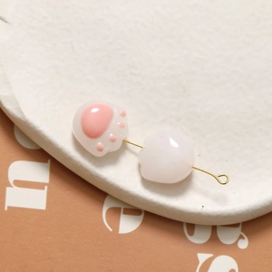 Detailed close-up of cute cat paw beads with glossy finish on a golden metal pin