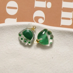 Detail of a transparent glass cat paw charm with green pads and a gold metal loop hook