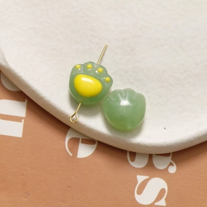 Macro shot of green resin cat paw charms with yellow pads and gold pins for DIY jewelry