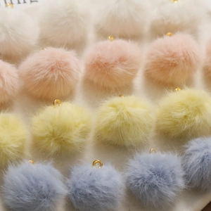 Dettaglio di pompon in ecopelliccia color pastello con anelli dorati per gioielli fai-da-te