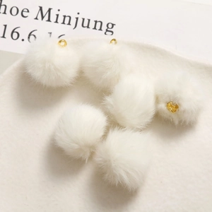 Dettaglio macro di sei pompon di peluche bianchi con ganci in metallo dorato per gioielli DIY