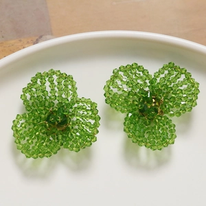 Detail of handmade green beaded clover earrings on a white ceramic plate