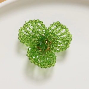 Macro shot of green faceted crystal beads hand-woven into a clover-shaped DIY accessory